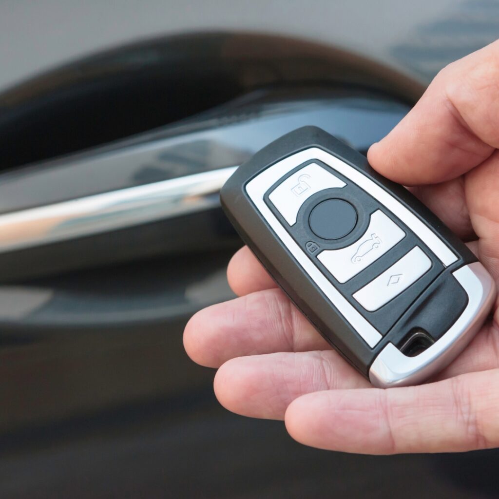 Hand holding a car key fob next to a car door.