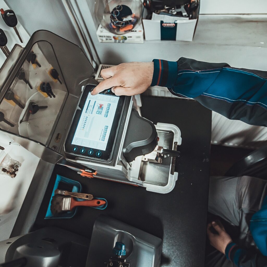 Hands operating a modern key cutting and programming machine.